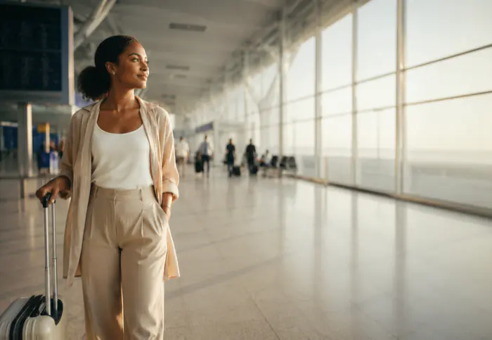 Une voyageuse traverse un hall d'aéroport, sa valise à la main.